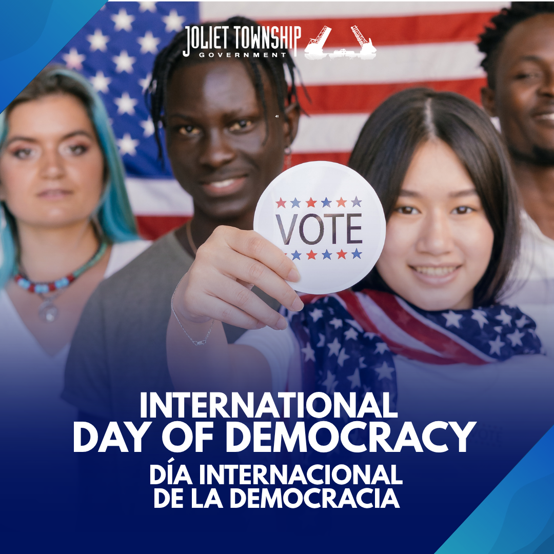 Four smiling people are standing in front of the American flag. One woman holds a button that says "Vote"